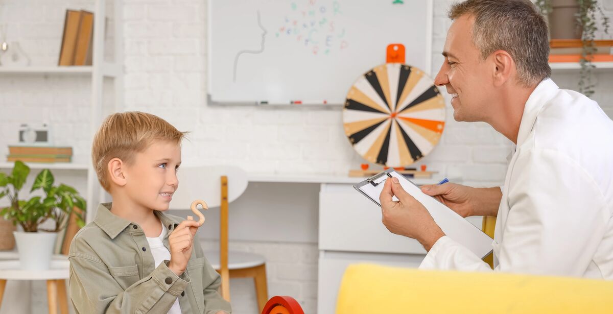 Little boy with speech therapist pronouncing letter S in office