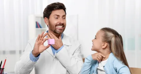 Speech therapist holding cube while working with girl at table in room